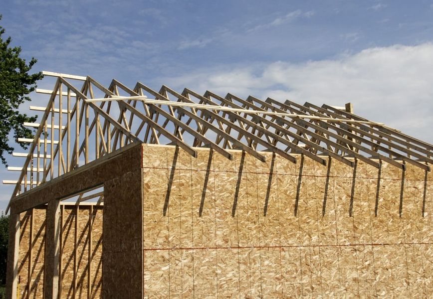 Wood frame building under construction, rafters in place on the roof, blue sky backdrop.