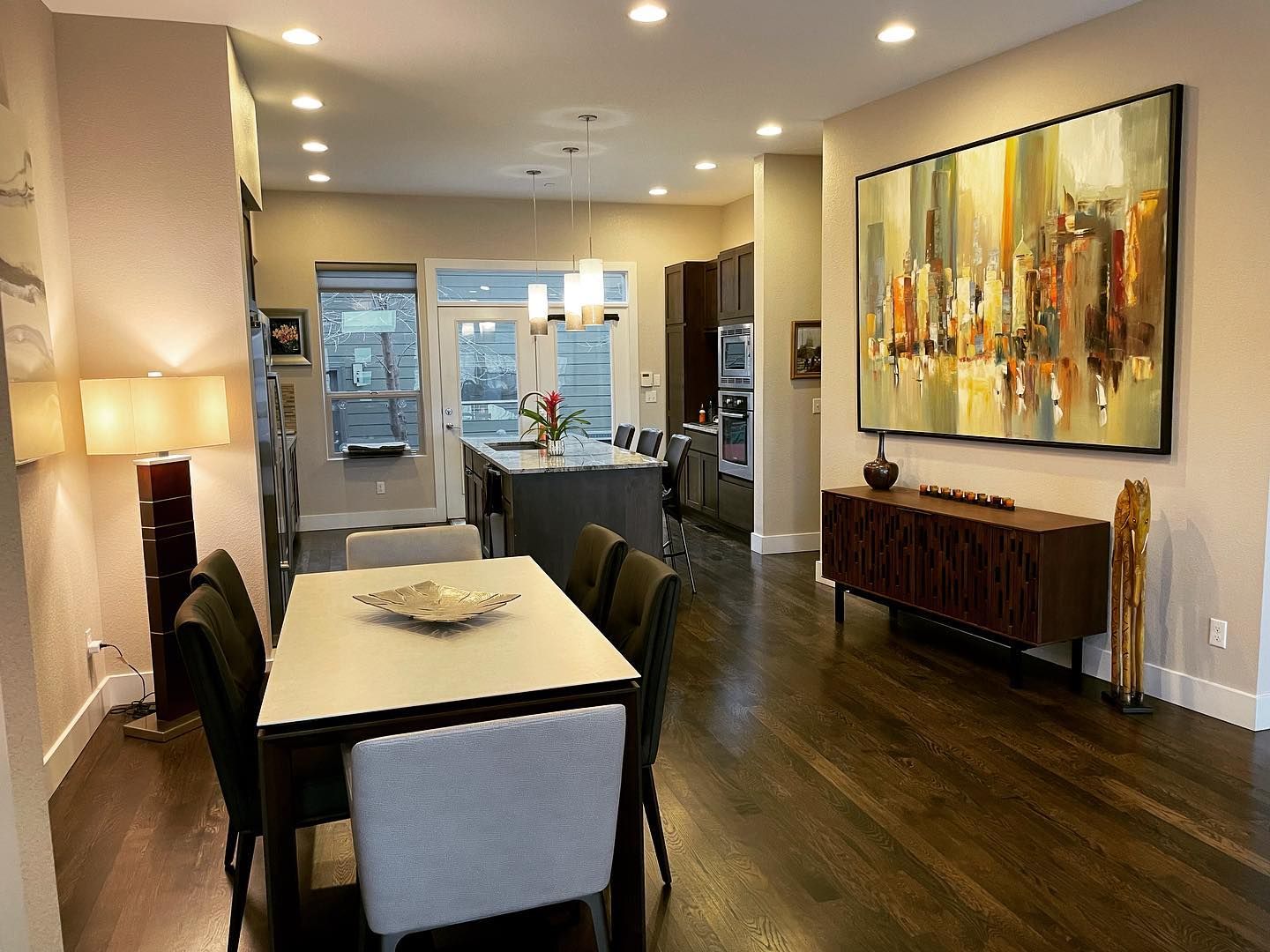 A dining room with a table and chairs and a large painting on the wall.