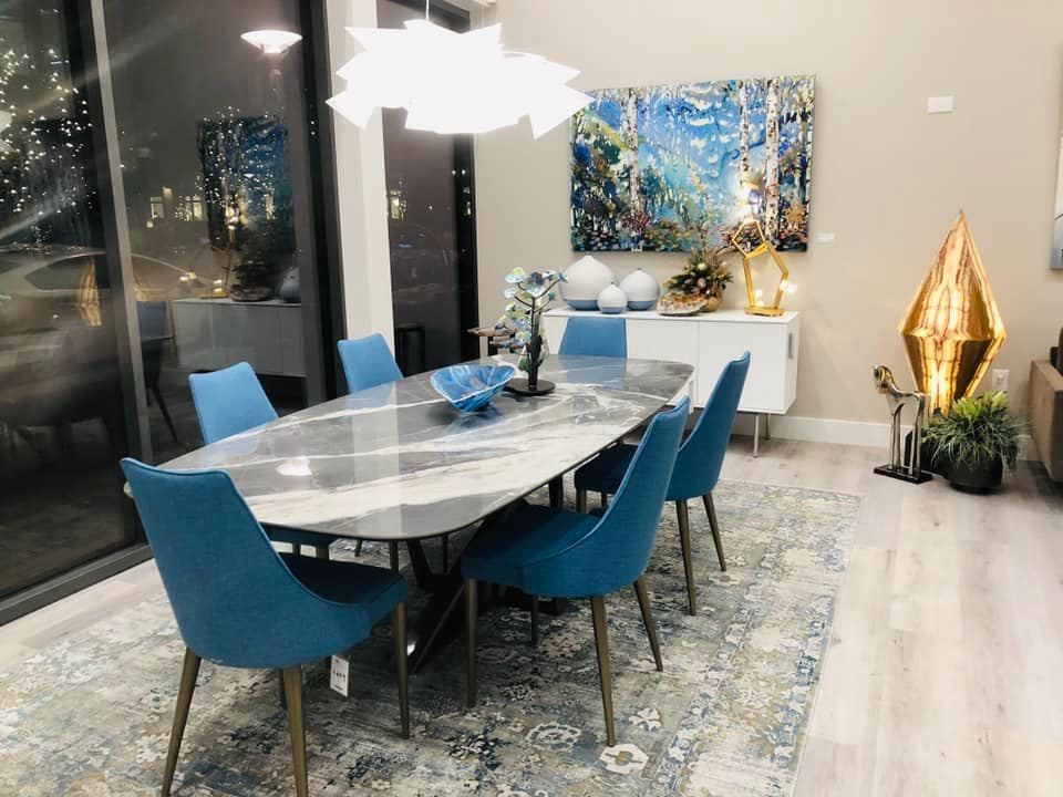 A dining room with a table and chairs and a painting on the wall.