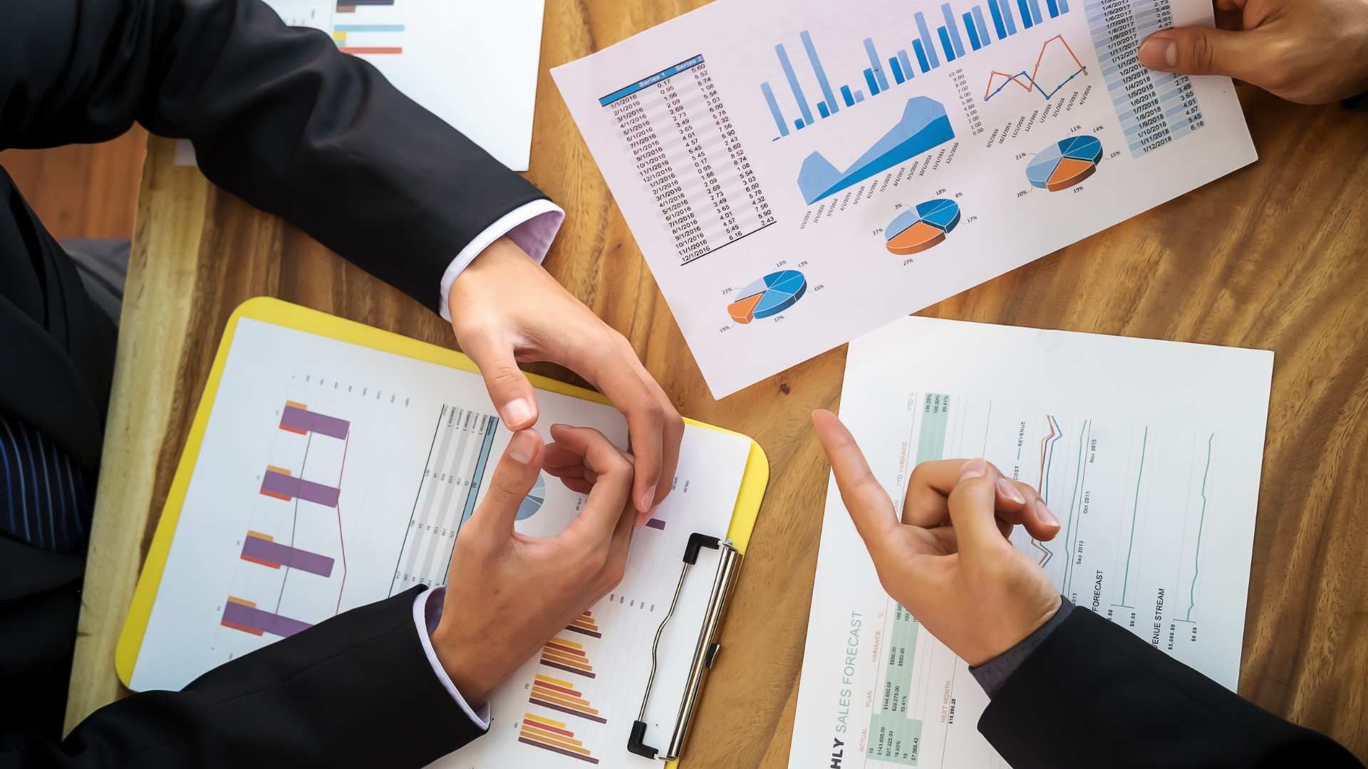 Business meeting with hands reviewing charts and graphs on printed reports at a desk