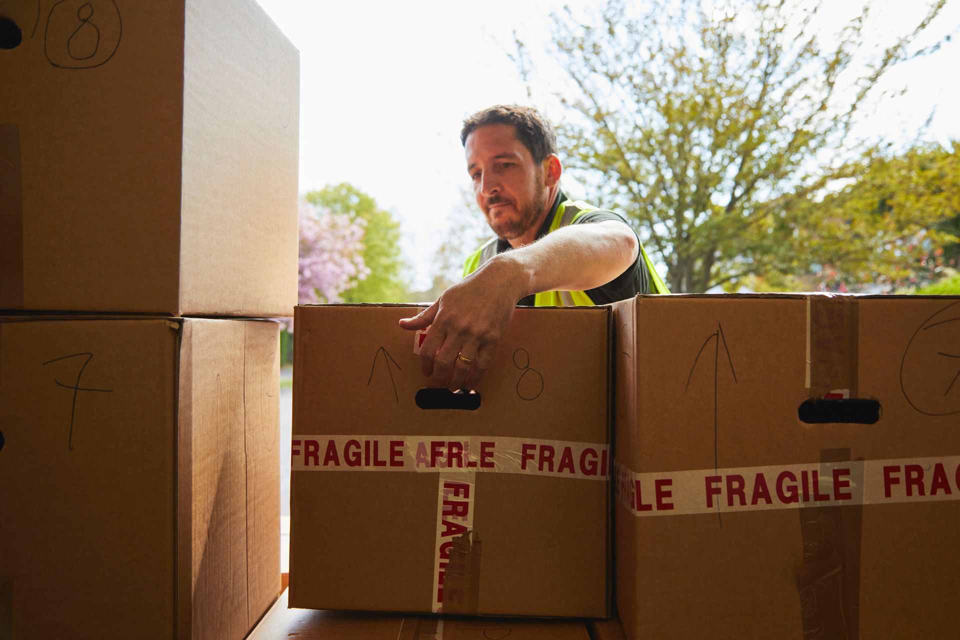 Man in a yellow vest handling a cardboard box labeled 