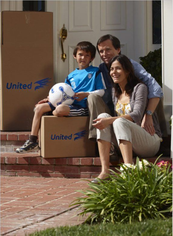 Family of three sits on front steps with moving boxes; boy holds soccer ball.
