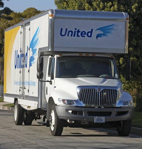White United moving truck on a street, blue logo, yellow and white accents.