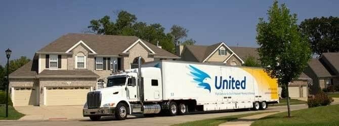 A white United moving truck parked in the driveway of a suburban house on a sunny day.