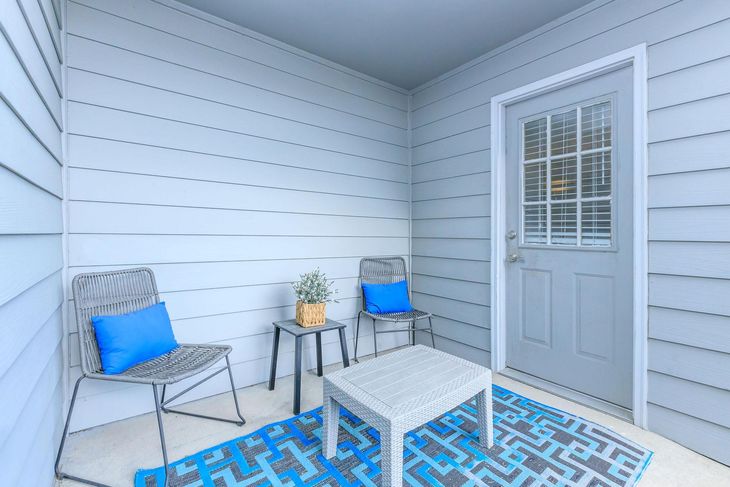 Small patio with two chairs, a table, and blue rug. A door is on the right.