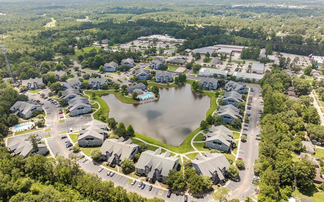 Aerial view of a residential community with a lake, surrounded by trees and buildings.