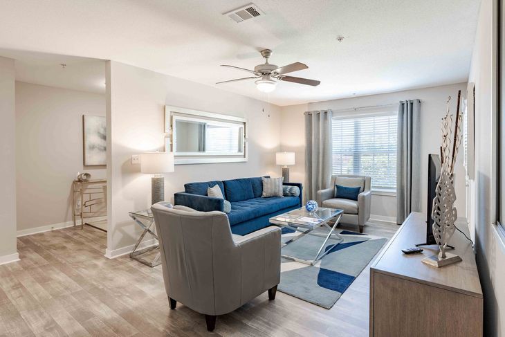 Living room with blue sofa, gray armchairs, and a TV in a bright apartment.