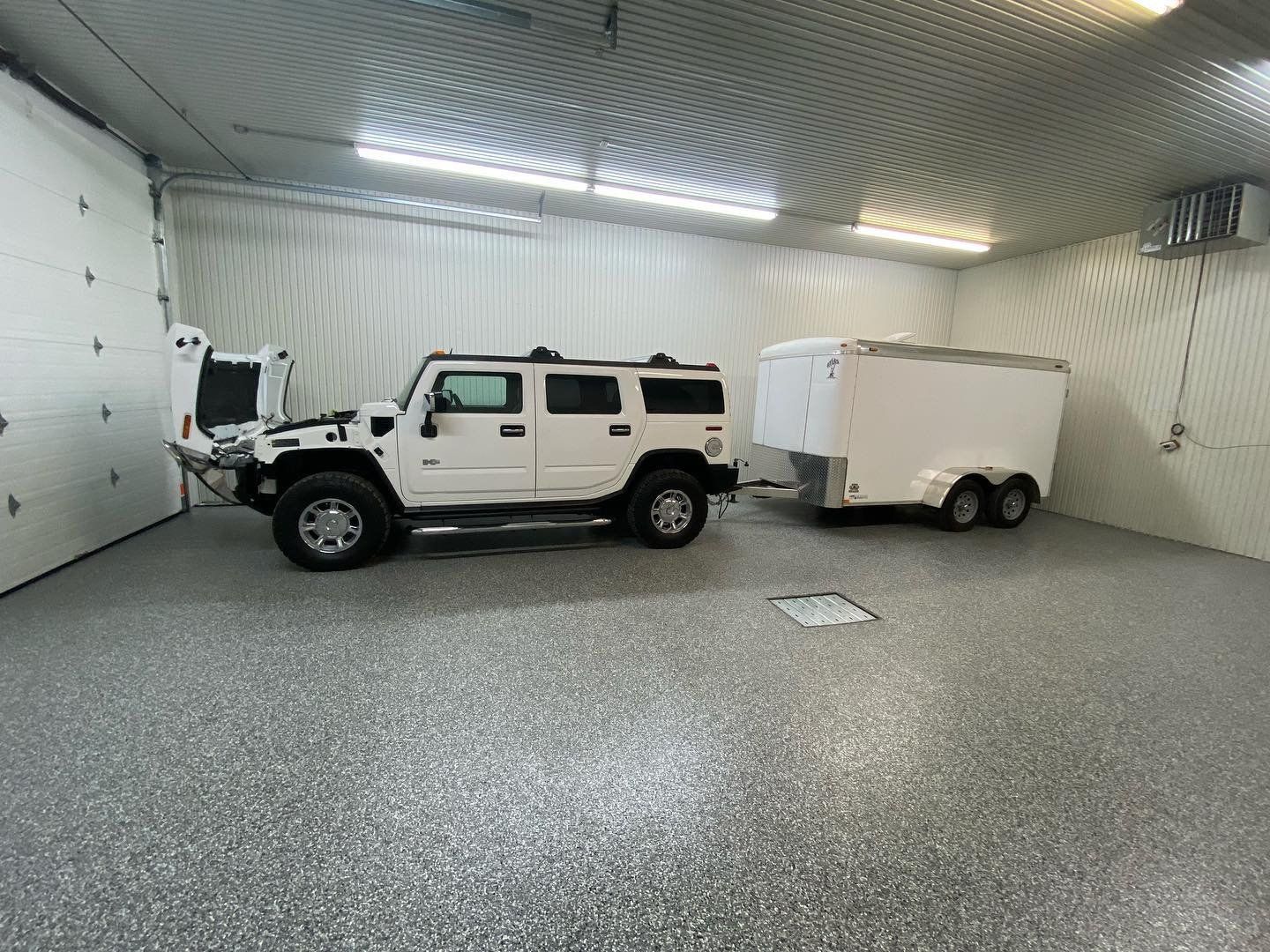 Un Hummer blanc est garé dans un garage à côté d'une remorque.