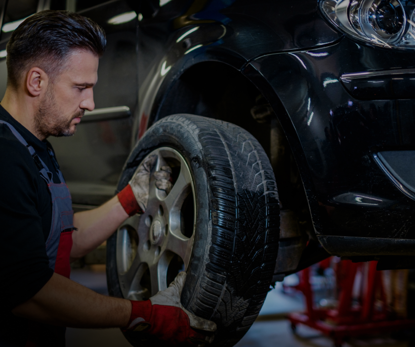 Mechanic removing a flat tire from a black car in a garage - OHMS Car Care & TOWING