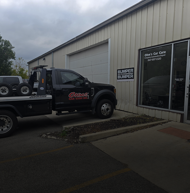 Black tow truck parked outside of a car care shop with a large garage door - OHMS Car Care & TOWING