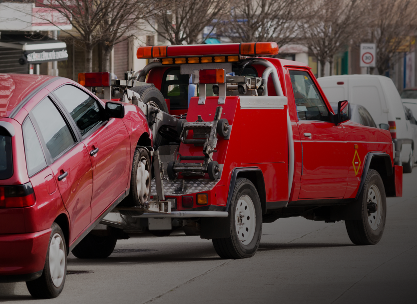Red tow truck towing a red car on a city street - OHMS Car Care & TOWING