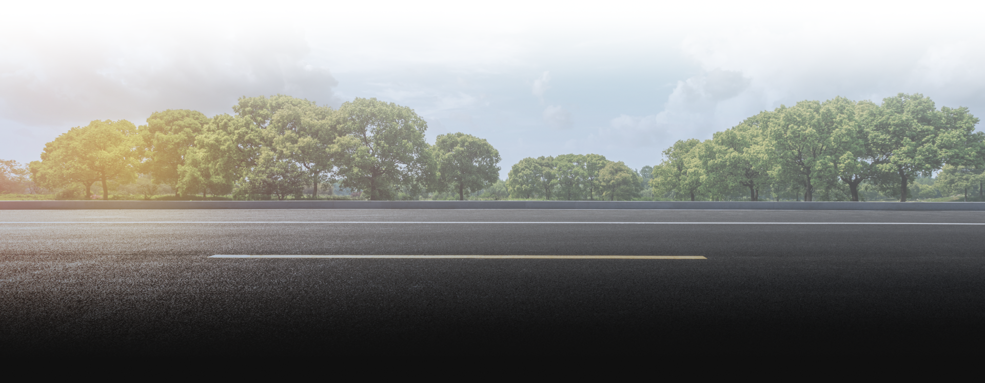 Asphalt road with a single lane divider, green trees, and a cloudy sky - OHMS Car Care & TOWING