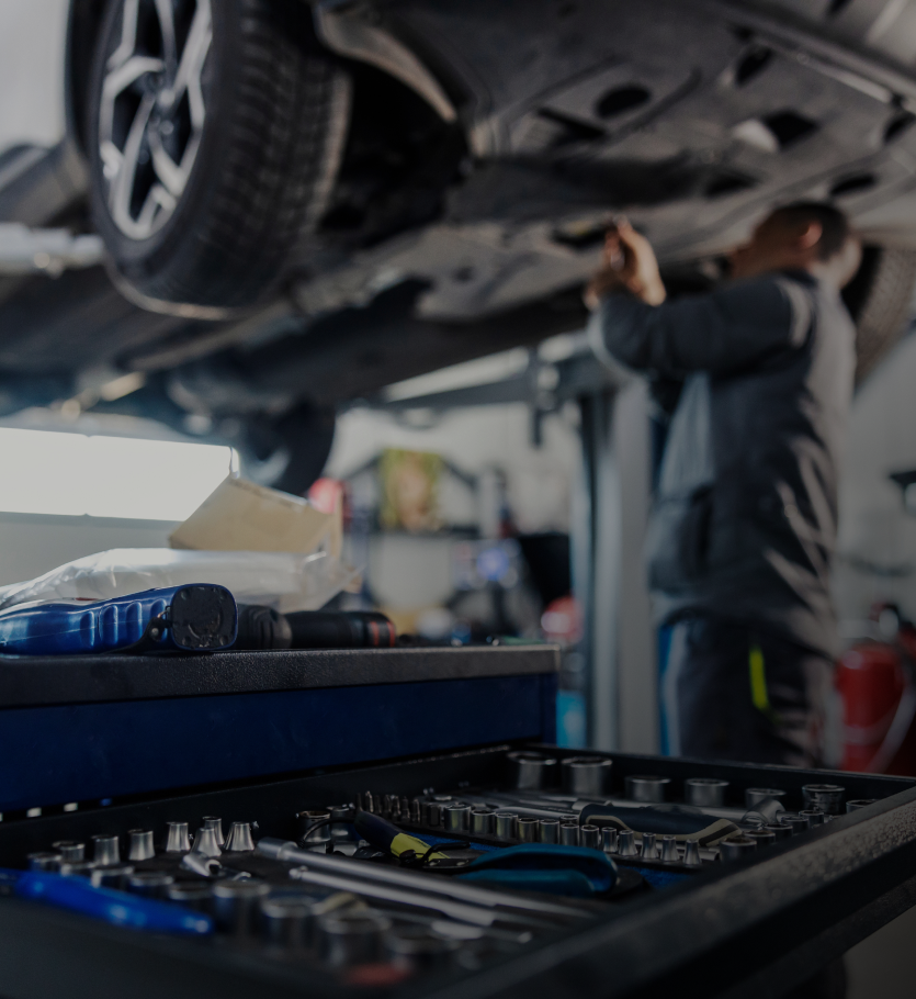 Mechanic working on car raised on a lift; tools in foreground, interior garage setting - OHMS Car Care & TOWING