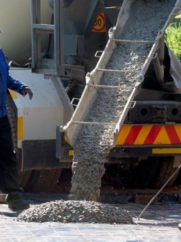 Concrete pouring from a truck into a pile on paving stones.