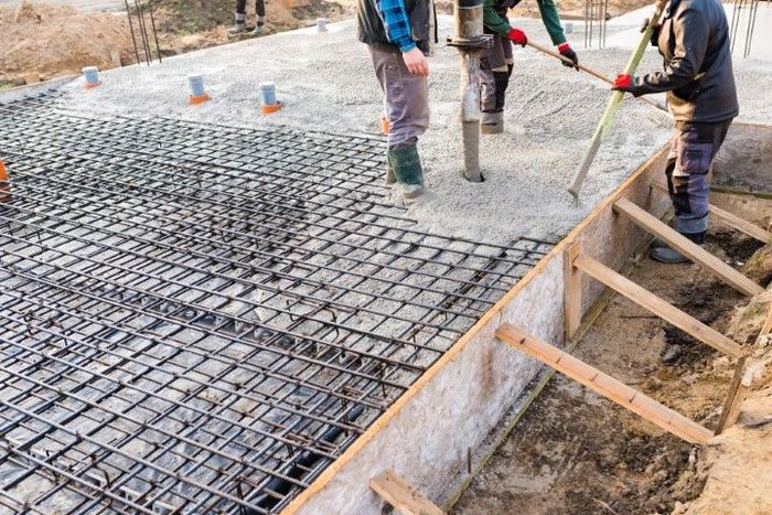 Workers pouring concrete over a steel rebar grid in a construction site.