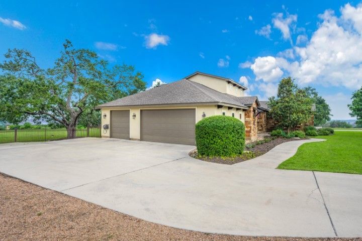 House with two-car garage and concrete driveway under blue sky with some trees.