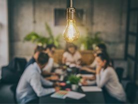 A group of people are sitting around a table with a light bulb hanging from the ceiling.