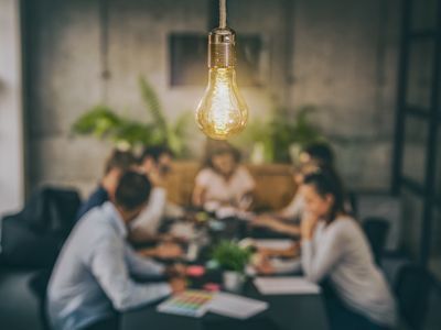 A group of people are sitting around a table with a light bulb hanging from the ceiling.