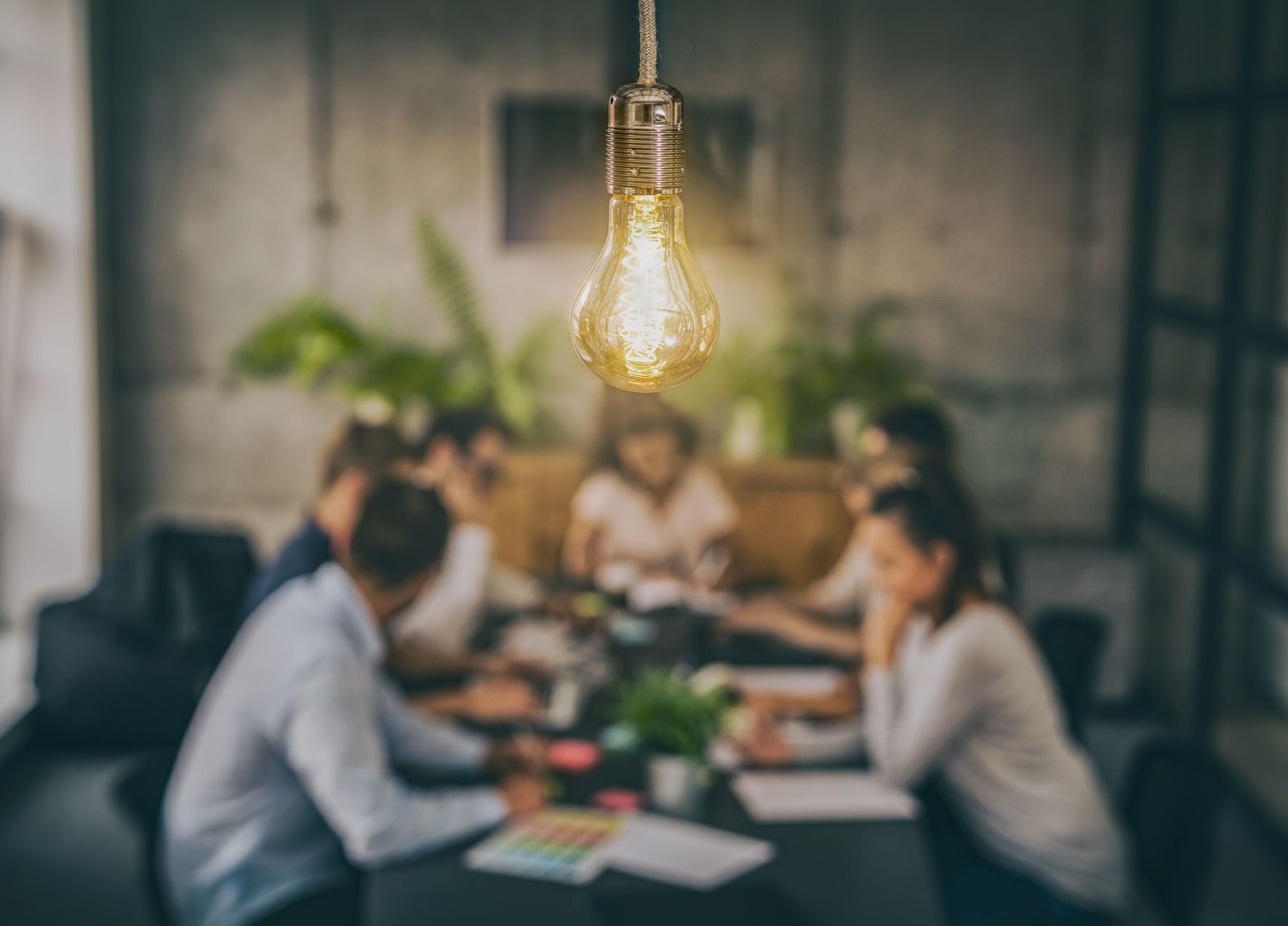 A group of people are sitting around a table with a light bulb hanging from the ceiling.