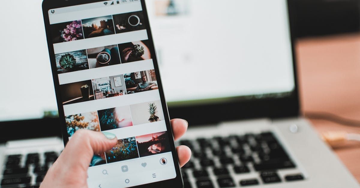 A person is holding a cell phone in front of a laptop.