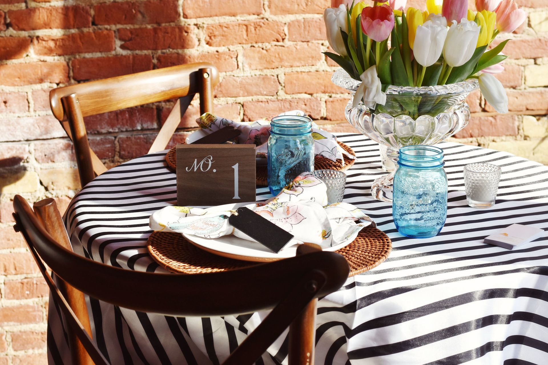 Table set for outdoor dining with striped tablecloth, flowers, and mason jars.