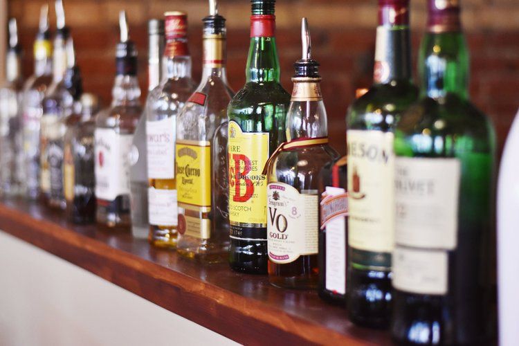 Bottles of liquor lined up on a bar. Some have spouts.