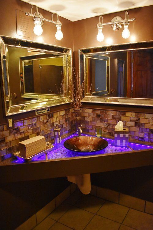 Bathroom with corner sink, mosaic tile, two mirrors, and purple under-cabinet lighting.