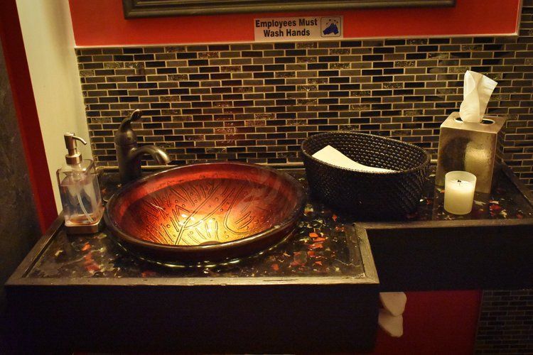 Dark, ornate bathroom sink with red and black accents, soap dispenser, tissue box, and candle.