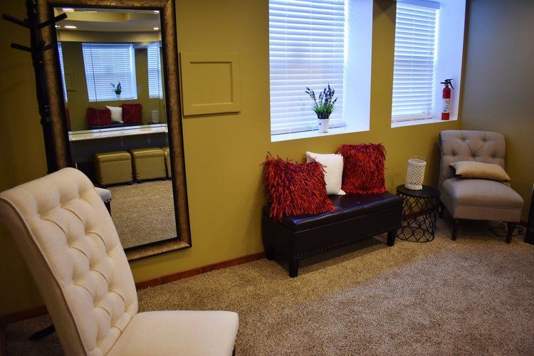 A waiting room with a mirror, chairs, bench, pillows, and a window with blinds.