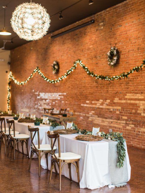 Reception hall with tables, white linens, chairs, brick wall, and string lights.