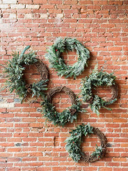 Five Christmas wreaths with greenery on a red brick wall.