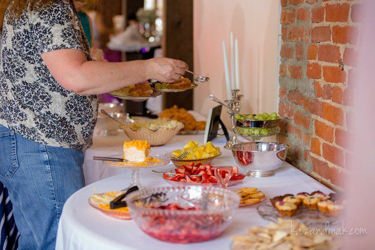 Person serving food from a buffet table; various dishes of fruit and snacks are displayed.