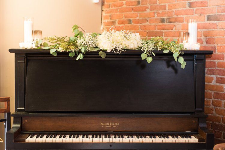 Black piano with floral garland and candles in front of a brick wall.