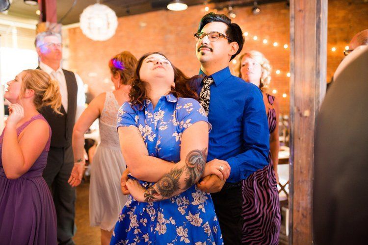 People dancing at a gathering. Woman in blue dress looks up while embracing a man in a blue shirt.