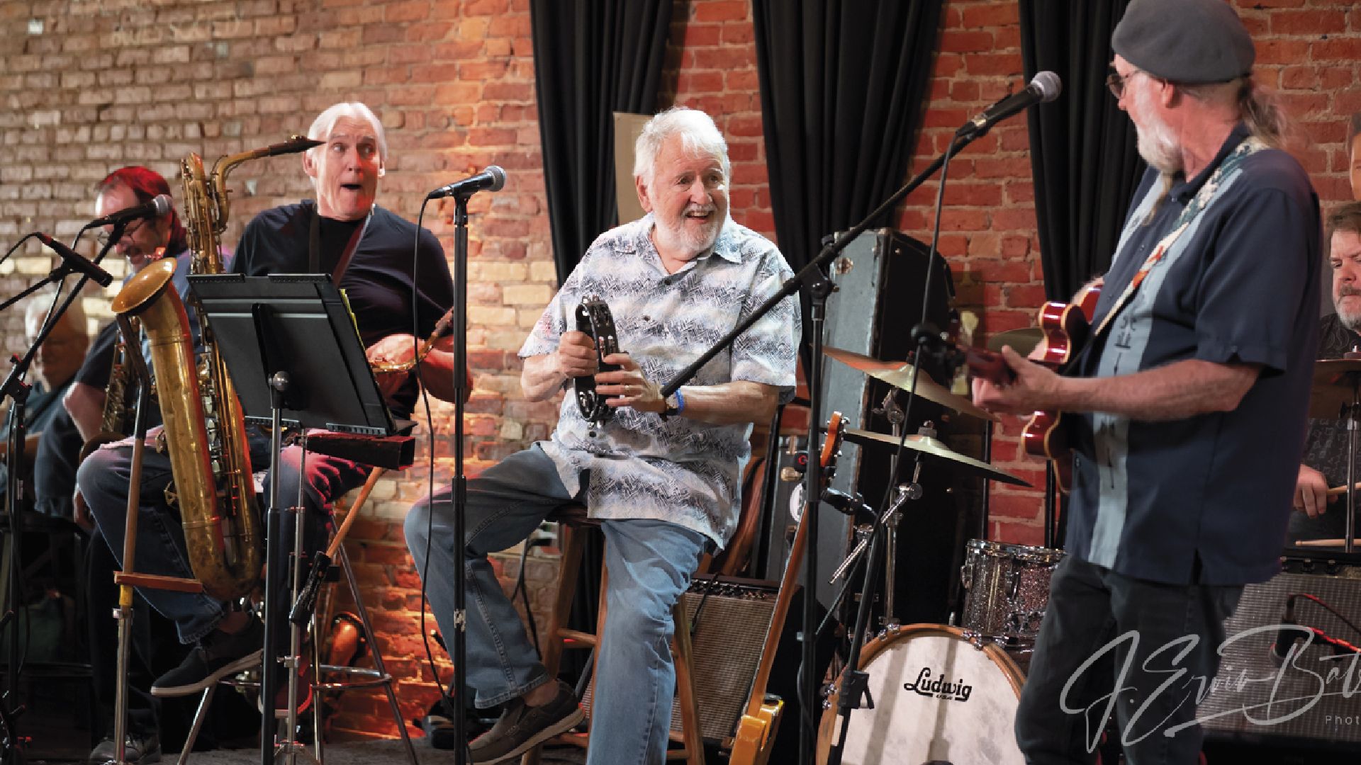 Four men playing saxophones on a stage, with microphones. They are performing in a dimly lit bar.