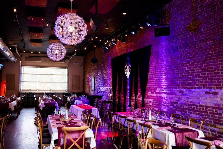 Inside a venue with tables set for a formal event, exposed brick wall illuminated in purple.