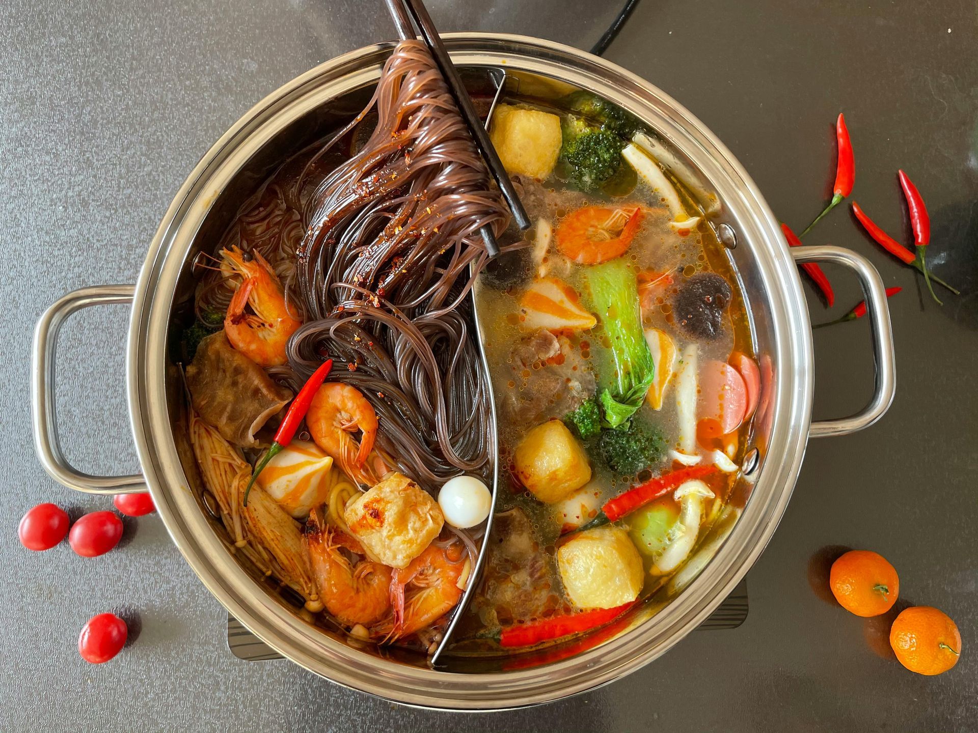 Spoon in a pot of colorful seafood and vegetables simmering in broth with chilies on a dark table