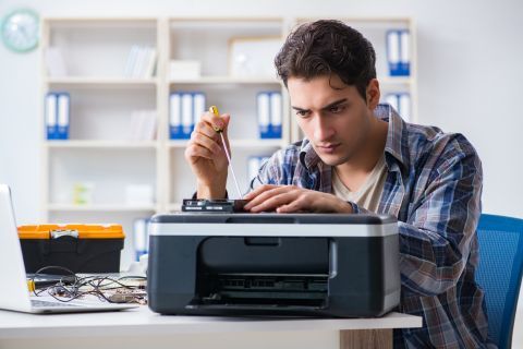 Un técnico concentrado en reparar una impresora, sosteniendo un destornillador en un entorno de oficina.