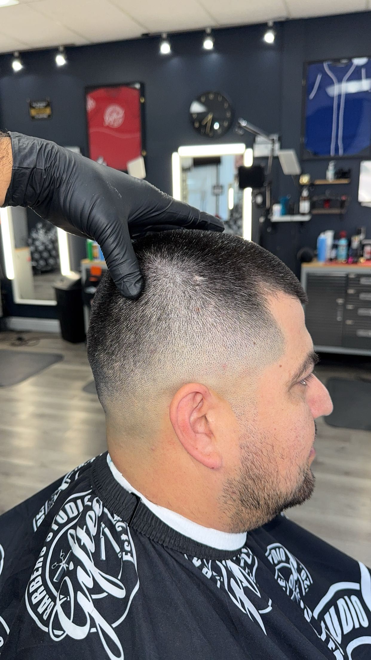 A man getting a fade haircut at a barbershop. The barber's gloved hand rests on the man's head.