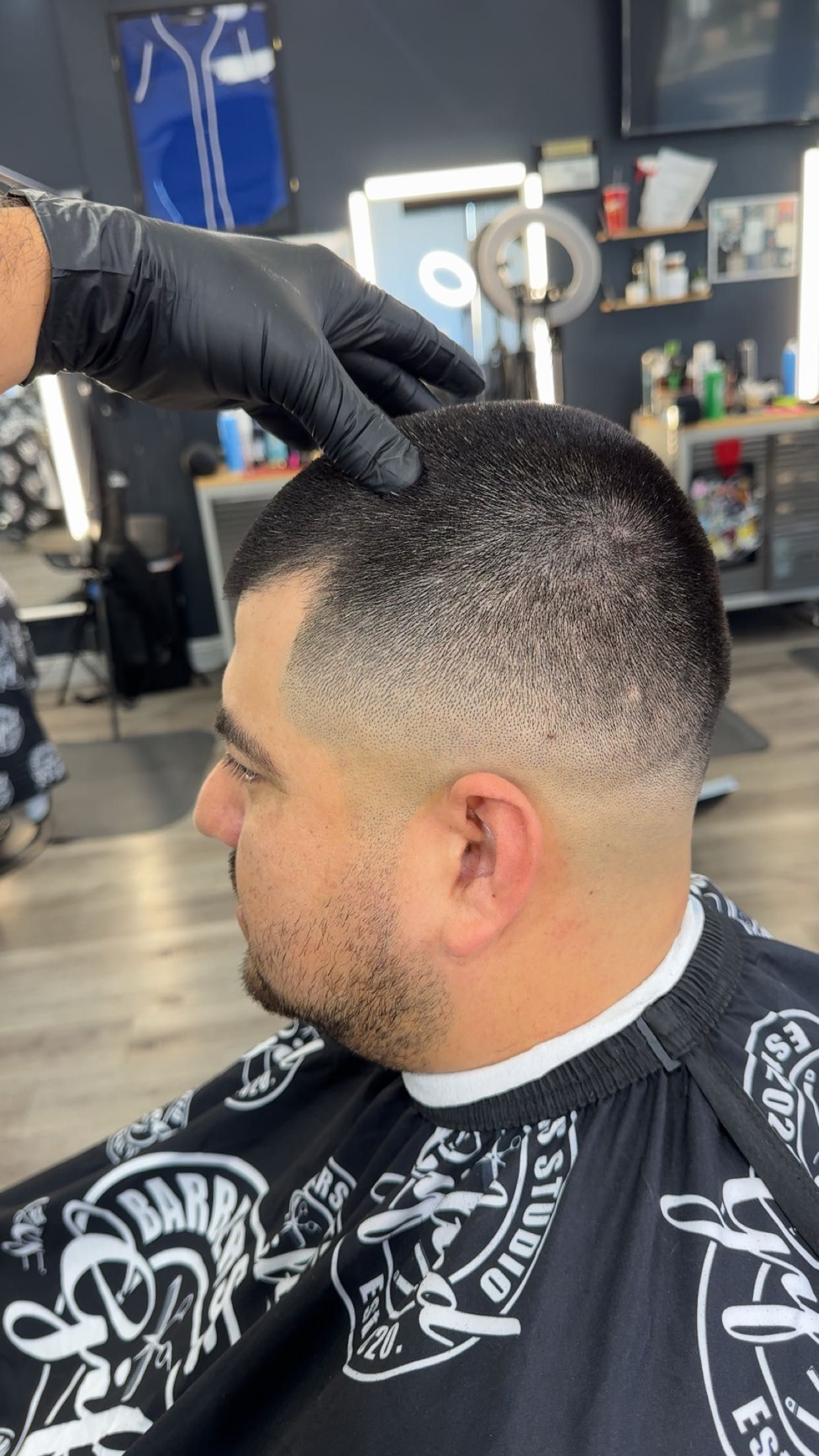 Man getting a haircut. Barber's hand touches the head. Fade haircut. Black cape. Inside a barbershop.