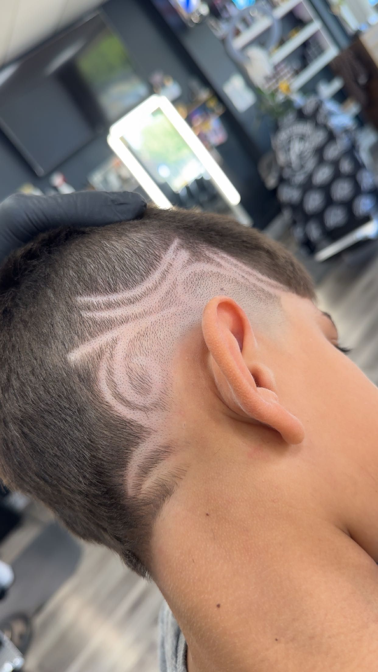 Person's head with a detailed shaved hair design near the ear, in a salon setting.