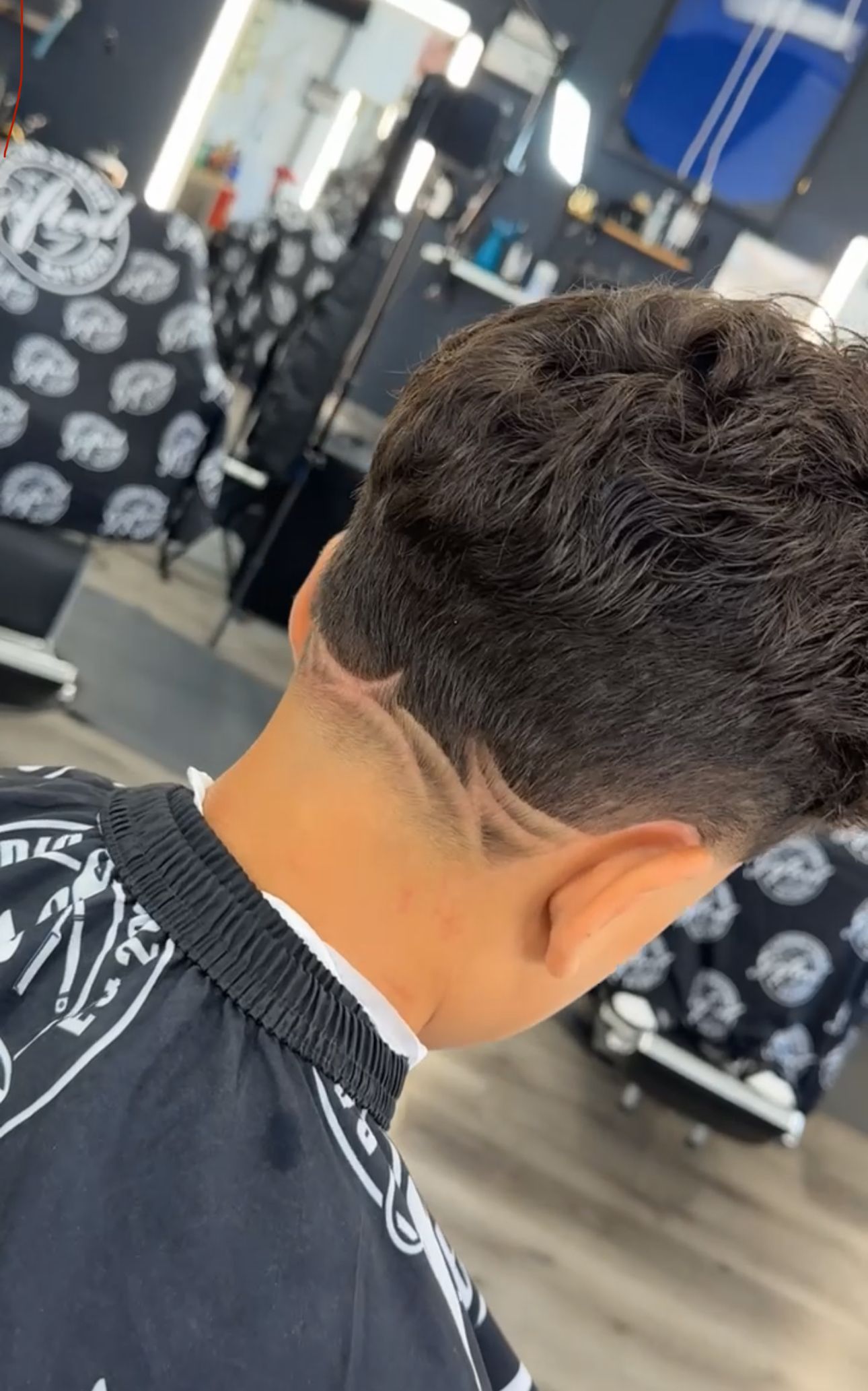 Close-up of a person's head with a detailed hair design on the neck in a barbershop.