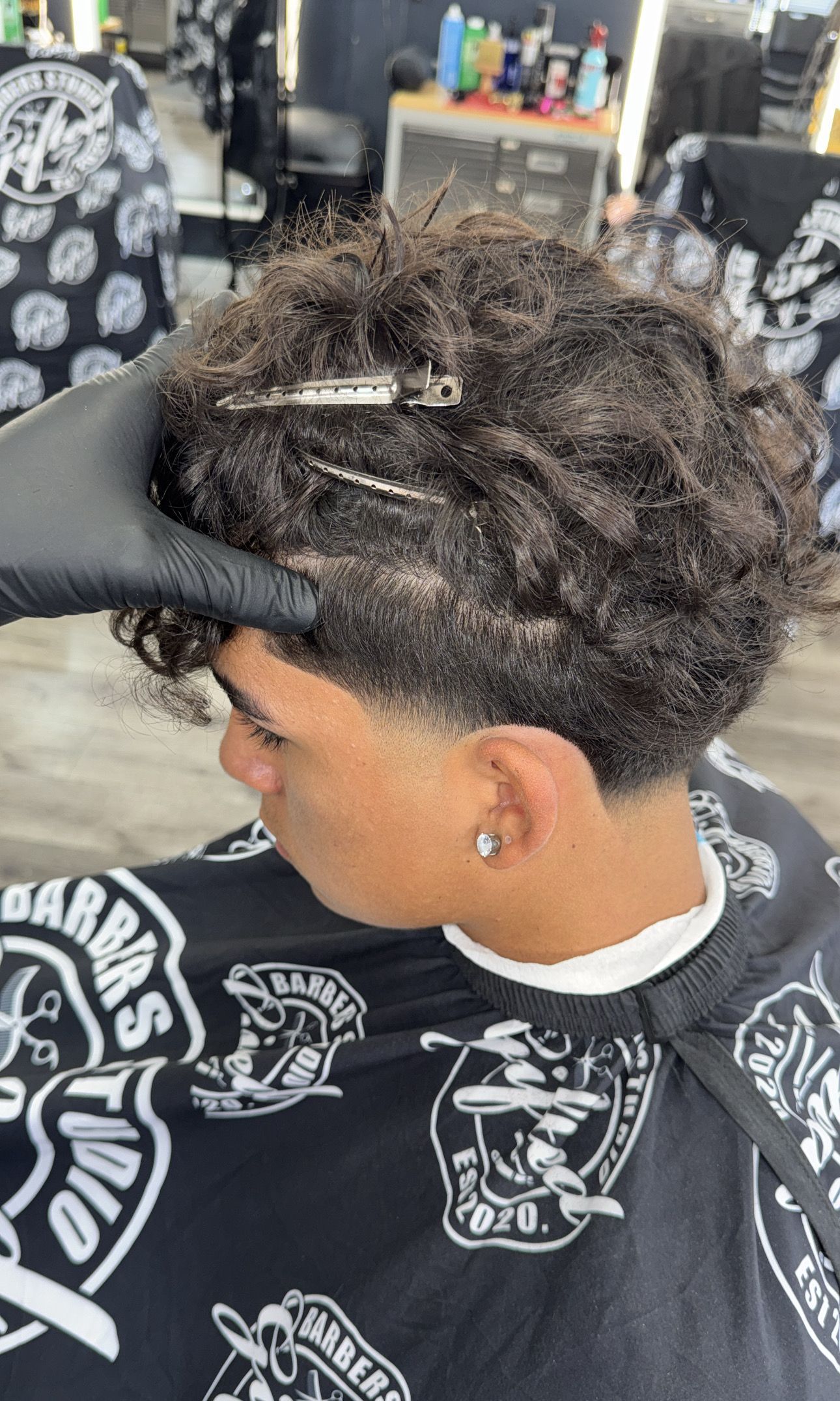 Person with curly hair, getting a fade haircut at a barbershop.