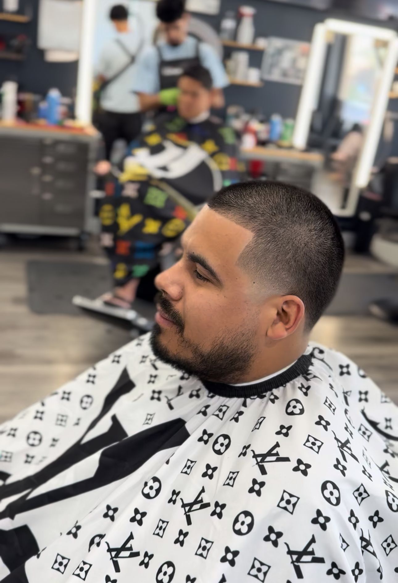 Man in barber chair getting a low fade haircut, wearing a Louis Vuitton cape.