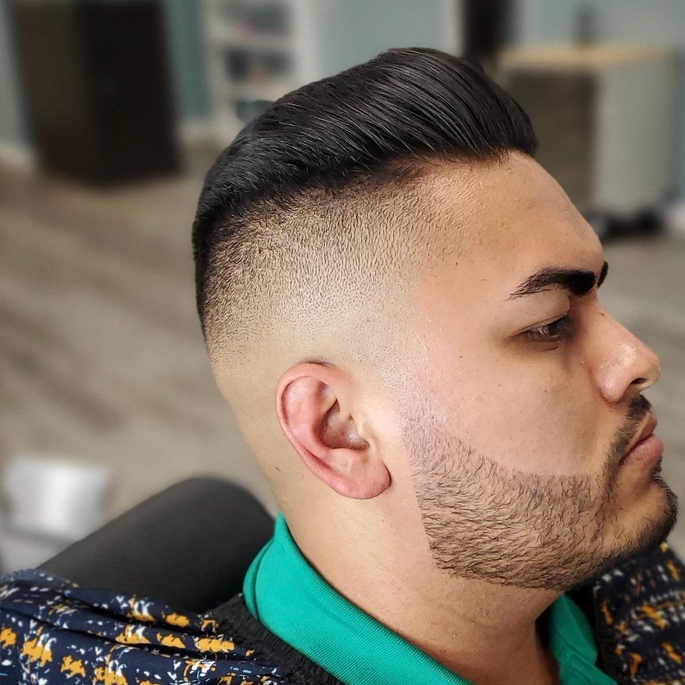 A man with a beard and a fade haircut is sitting in a chair.