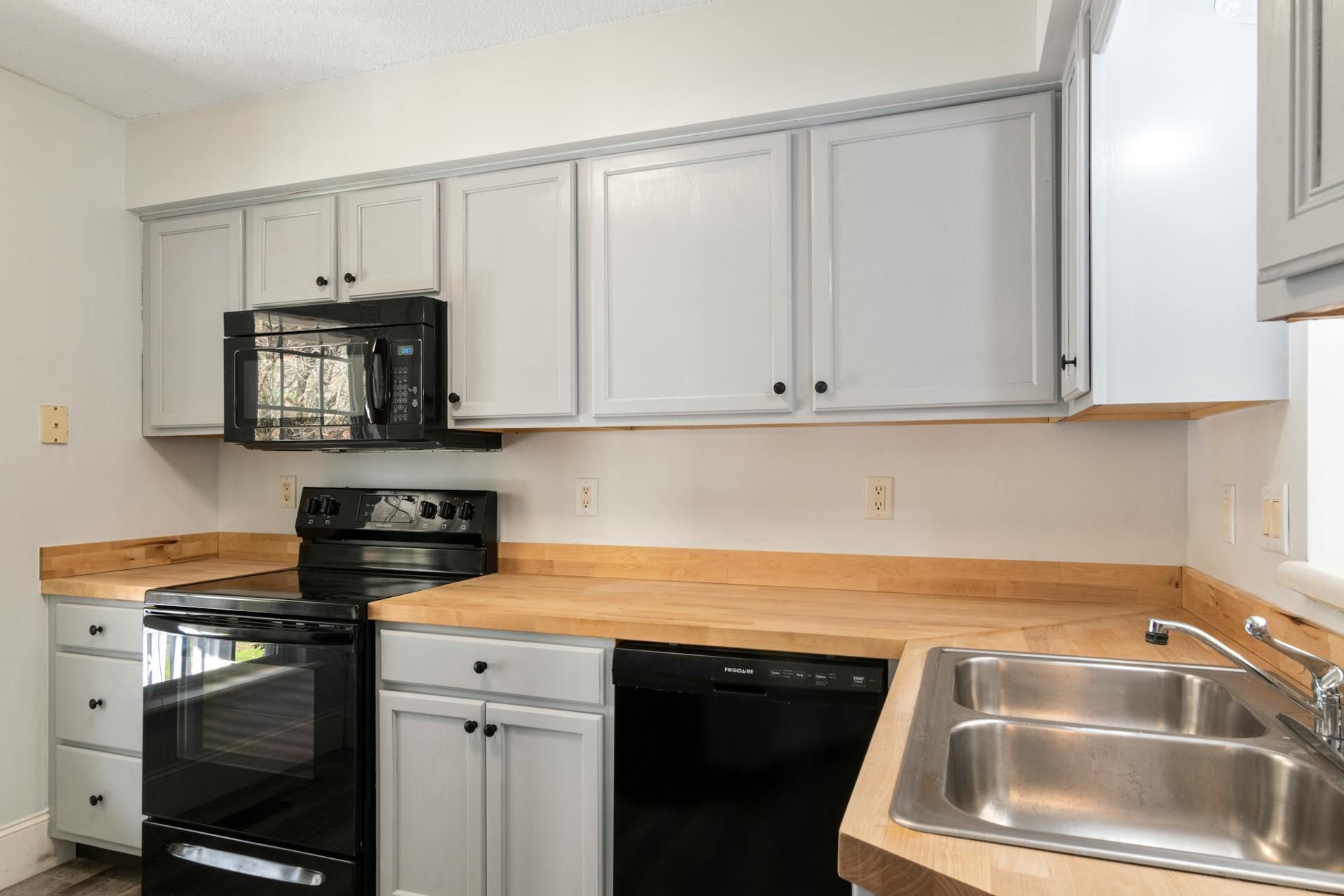 A kitchen with white cabinets , black appliances , a sink , and a microwave.