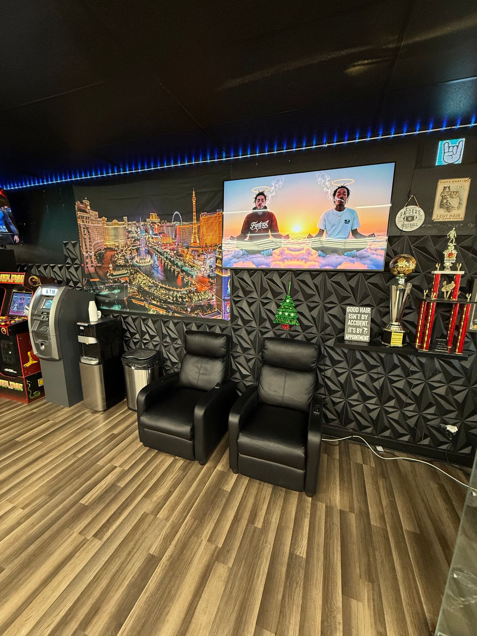 Two black chairs face a TV in a game room with cityscape art, trophies, and arcade games.