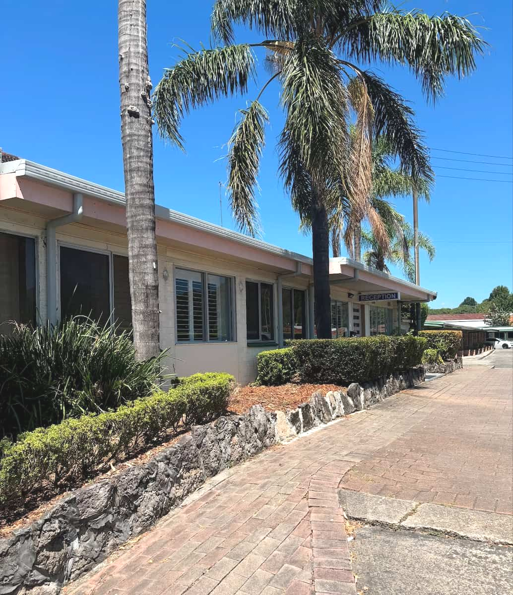 A Light-colored, Single-story Building Sits Behind a Stone — Crystal Clear Plumbing & Roofing in Wollongong, NSW