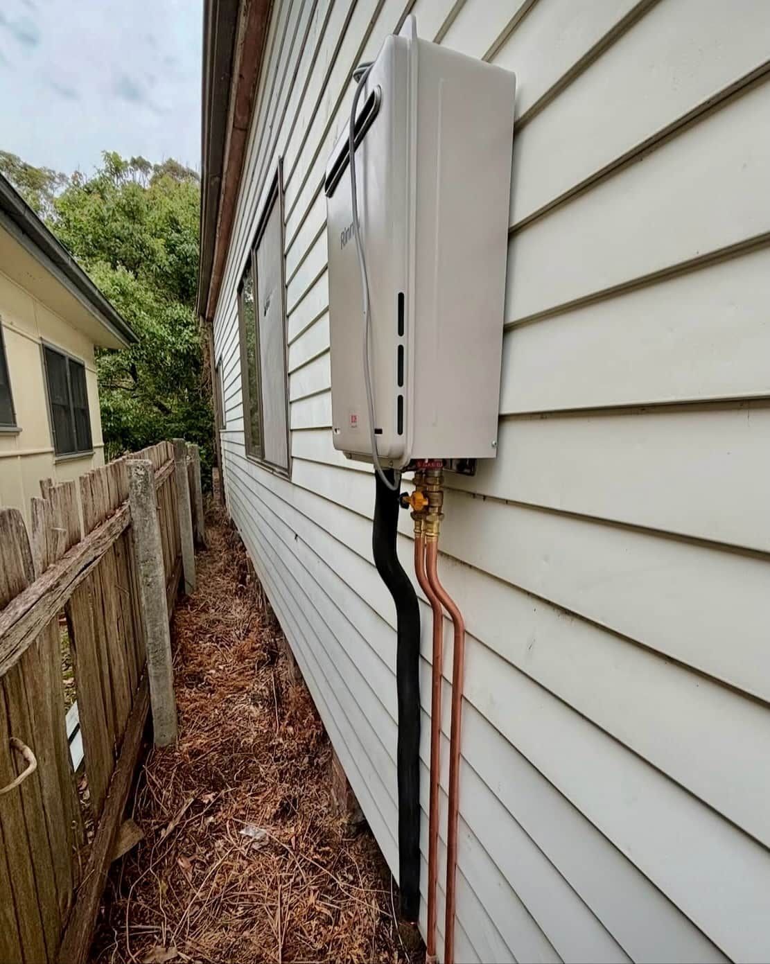 An Off-white Tankless Water Heater Mounted on the Exterior Wall — Crystal Clear Plumbing & Roofing in Wollongong, NSW
