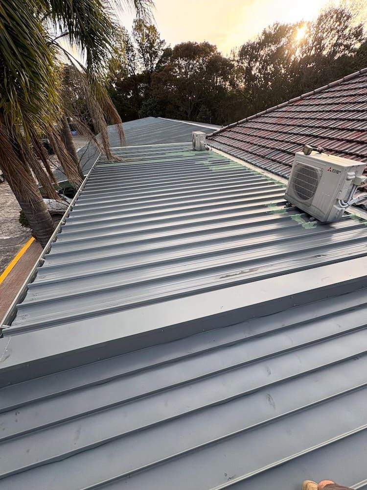 A High-angle View of a Grey Metal Roof With a Small Outdoor HVAC Unit — Crystal Clear Plumbing & Roofing in Wollongong, NSW